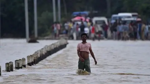 Getty Images A villager is walking through a flooded road after heavy rainfall in Hojai District of Assam, India, on July 5, 2024