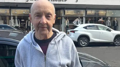 A man standing in the street holding a paper bag wearing a grey hoodie