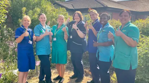 Nurses at Prospect Hospice standing outside the hospice building in Wroughton with their thumbs up.