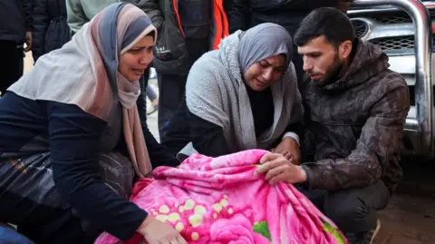 Reuters Mourners crouched with the covered body of a Palestinian killed in an Israeli air strike in Gaza (03/01/25)