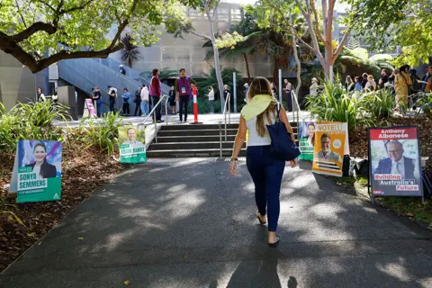 Getty Images From the back woman walks up a dark path next to it with election placards on the side, towards a group of people