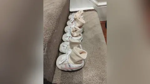 Three pairs of identical baby shoes and socks lined up along a carpeted stair 