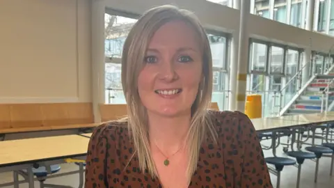 A woman with blonde hair and an animal print shirt is looking face on to the camera