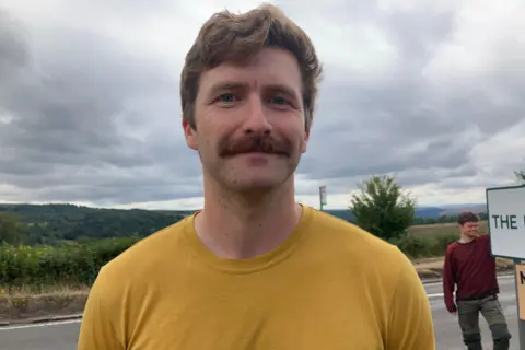 A man with brown hair and a mustache in a yellow t-shirt.