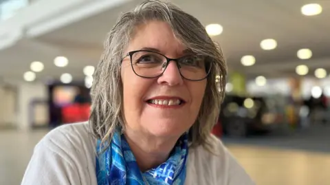 BBC Pat Pengelley - A woman with grey hair, glasses wearing red lipstick. 