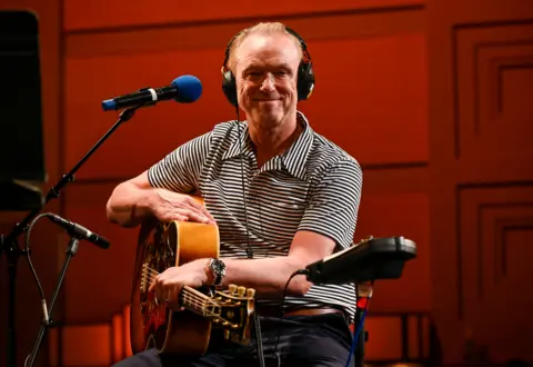 Gary Kemp in a stripy top sitting with a guitar