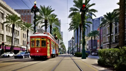 A red tram in New Orleans' French Quarter, with palm trees lining both sides of the road