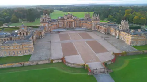 Gambar istana barok yang sangat besar terlihat dari langit. Ada ladang hijau di sekitar istana. 