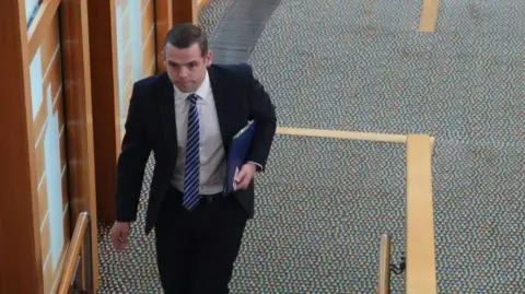 Douglas Ross walks along a corridor carrying a folder