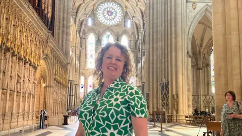 Laura is pictured in a green and white dress in front of the Minster's rose window