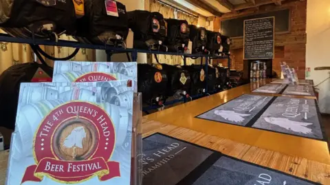 QUEEN'S HEAD BRAMFIELD  Barrels of real ale are stacked beside a bar with beer mats on and leaflets for beer festival