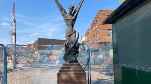 The Phoenix statue displayed in Coventry city centre as demolition work happens behind it. The statue has fences around it.