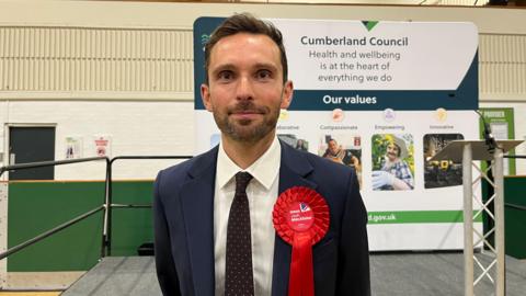 Winning Labour candidate Josh McAlister wearing a blue suit and a red rosette