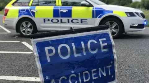 BBC Police vehicle parked behind a blue police accident sign 