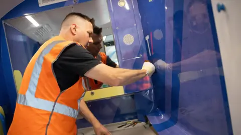 Thameslink A man in an orange hi-viz installs a vinyl wall.
