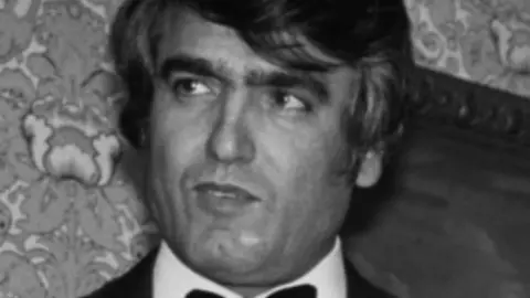 AFP via Getty Images A black and white image of Ahmed Obaidly looking to his right. He has floppy dark hair and is wearing a suit and tie.