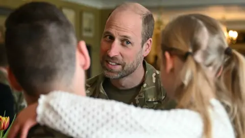 Justin Tallis/PA Wire Prince William smiling slightly at a man holding a young girl in his arms