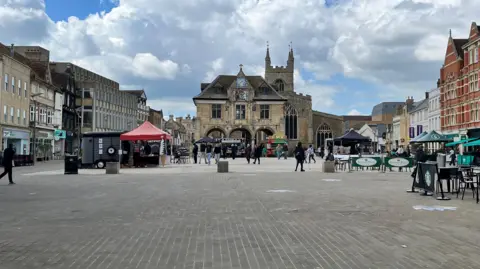 Emma Baugh/BBC The modern-day Cathedral Square with market stalls and table and chairs, and the Guildhall in the background.