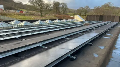 Drax A set of solar panels on the roof of an old hydro power plant with trees and hills in the distance