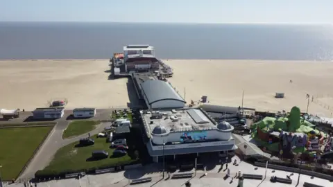 Jamie Niblock/BBC A drone image of the Britannia Pier stretching along the sandy beach, with the sea in the background. The theatre is at the end of the pier. 