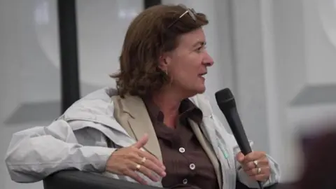 Eluned Morgan holding a microphone and wearing a white jacket and beige top