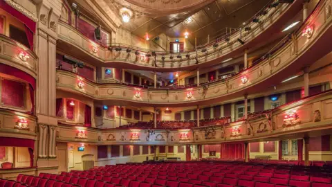 Morley Von Sternberg The ornate theatre interior has rows of red seats, curved balconies, decorative plasterwork and warm lighting viewed from the stage towards the auditorium