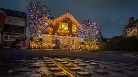 Getty Images A house is lit up in colourful Christmas lights on a residential street. It has yellow lights all over it, creating a waterfall-like effect in places. Two trees outside the property have been covered in coloured lights.