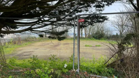 Overgrown tennis courts with a high metal fence in front of them