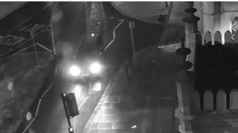 Sussex Police A black and white CCTV image of a car on a road.