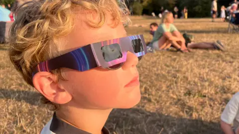 Handout A young boy is wearing special eclipse glasses while looking at the sun