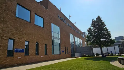 Paul Moseley/BBC Red brick building with black letters spelling out Norfolk and Norwich University Hospital across the bricks, and an NHS sign in white on blue 