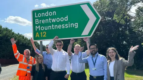 Seven team members from Morgan Sindall and National Highways cheering next to a road sign