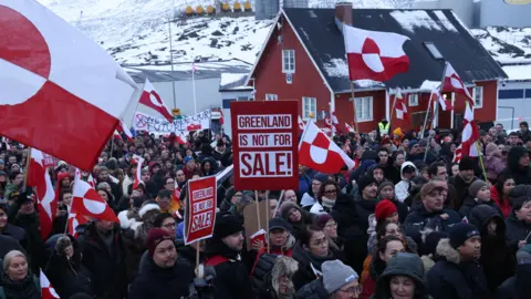 People hold Greenlandic flags and placards as they gather by the United States Consulate to march in protest against U.S. President Donald Trump and his announced intent to acquire Greenland.