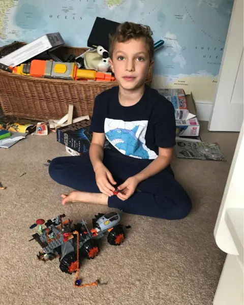 Family handout A young boy around eight years old is sat crossed legged on his bedroom floor. A mechanical lego vehicle is in front of him. He is looking into the camera. 
