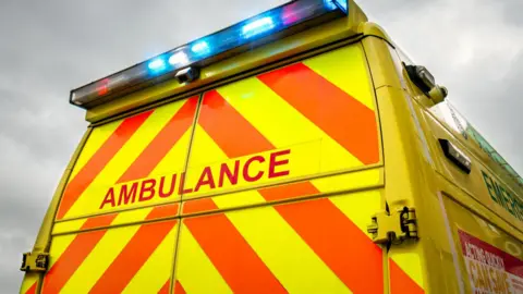 The rear view of an ambulance - a yellow vehicle with orange stripes