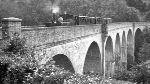 A black and white image of a train travelling over the viaduct. 