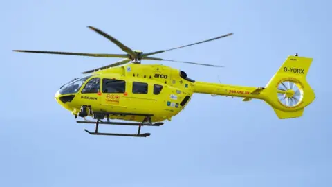 Yorkshire Air Ambulance, a yellow helicopter, in a blue sky.   