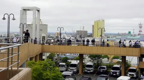 Reuters stand on a raised infantry bridge, at the top of the parking lot. They are looking for the city.