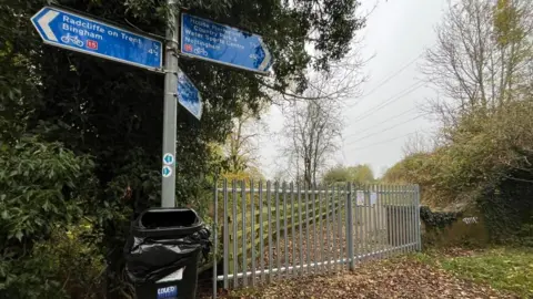 A view of the fence which has closed the cycle path, with a nearby cyclist directions sign.