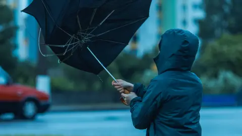 Anonymous person in raincoat with erect umbrella being battered by wind outdoors