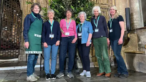 Canterbury Cathedral Flower Guild members Valerie Hale, Dee Hickman, Margaret's Carnegie, Rosie Corteen, Jane Wilson and Lucy Day stand next to one of their sustainable 'bloomless' arrangements in the Nave
