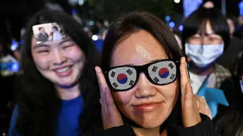 Supporters of Lee Jae-myung, the presidential candidate for South Korea's Democratic Party, shout slogans, with one wearing sunglasses adorned with the national flag.