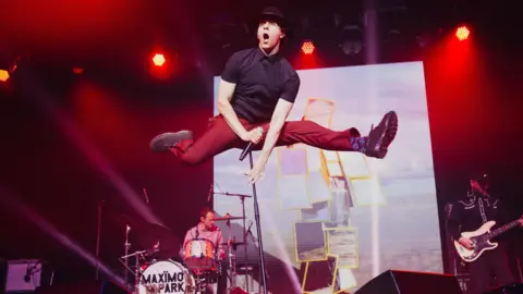 Isle of Wight Festival Maximo Park frontman in mid-jump on stage at the Isle of Wight Festival