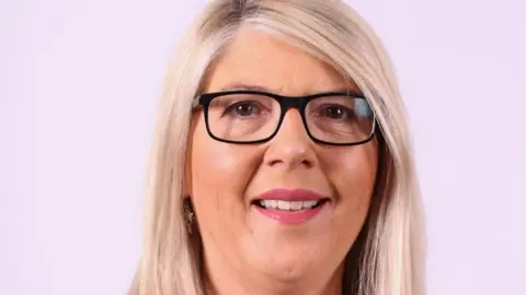 A woman with blonde hair and dark framed glasses