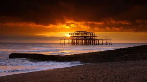 A burnt out pier on the beach, illuminated by sunset