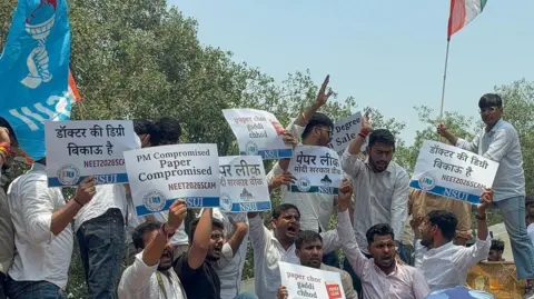 Protesters standing on barricades holding placards which read the medical entrance test is compromised as police personnel push them back