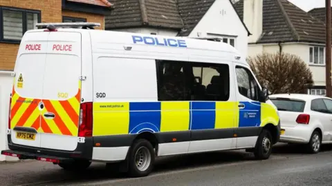 A police van parked on a road in Watford. There are detached houses behind it.