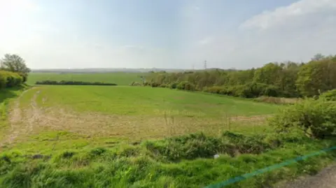 A green field site with a rural road alongside 