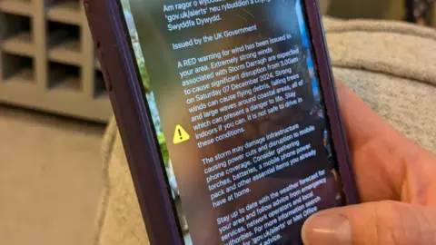 BBC An image of a phone in a hand. On the screen is a message for the red weather warning. 