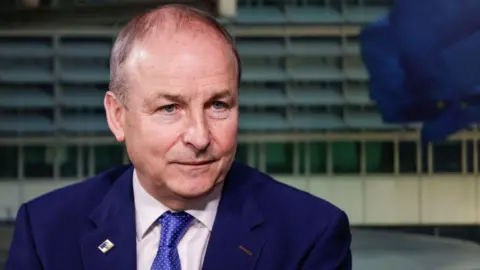 Getty Micheál Martin sits satring off camera. He is wearing a navy suit, white shirt and a blue tie with a pin on his lapel.